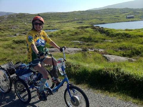 Susan Sygall riding adaptive bike with three wheels through meadow