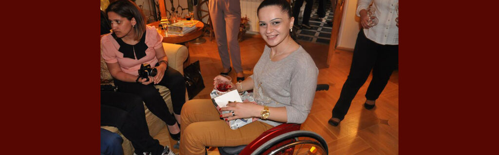 A young woman using a bright red wheelchair smiles at the camera.