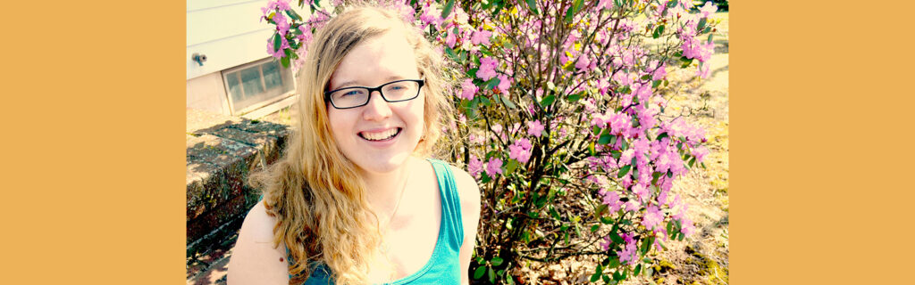 Courtney Thompson smiles broadly in front of blooming bush