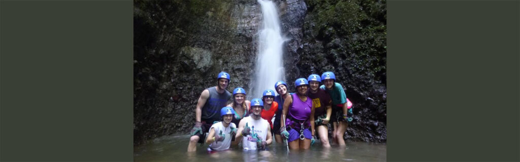 Juanita standing under waterfall with friends.