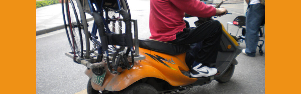 Wheelchair strapped to the back of a motor scooter.