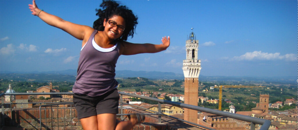 A girl smiles in mid-year at a point overlooking a city in Italy.