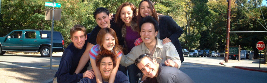 A group of students from different countries, including a student in a wheelchair, share a group hug.