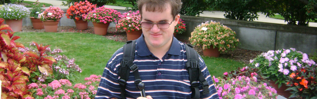 A blind man sits near a flower-filled landscape.