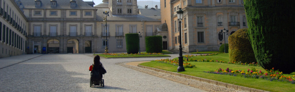 A women using a power-wheelchair wheels in front of historic buildings in spain.