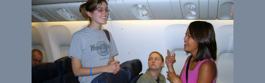 Two Deaf women communicate with each other in sign language on an airplane.