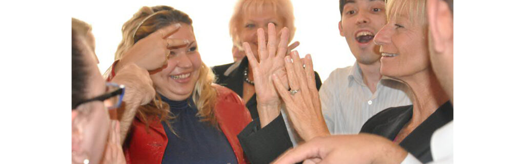 A group of people are gathered and demonstrating different signs while smiling.
