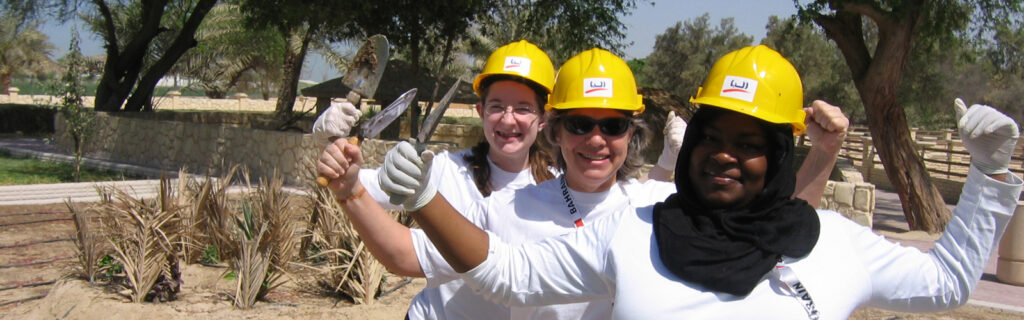Three women in hardhats holding up gardening tools