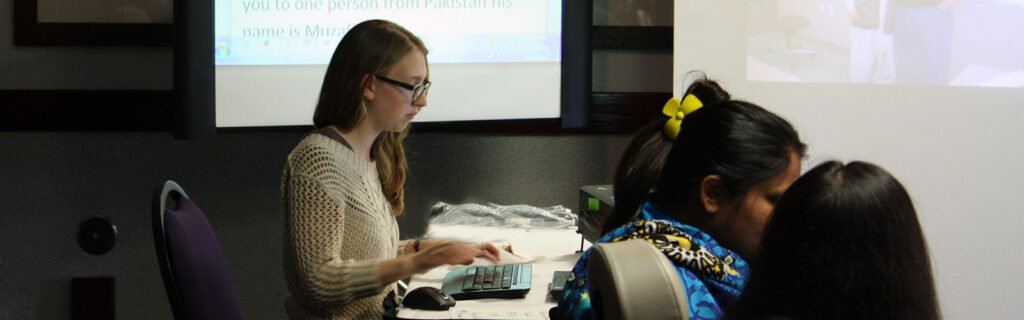 A young woman types on a computer with projector screens.