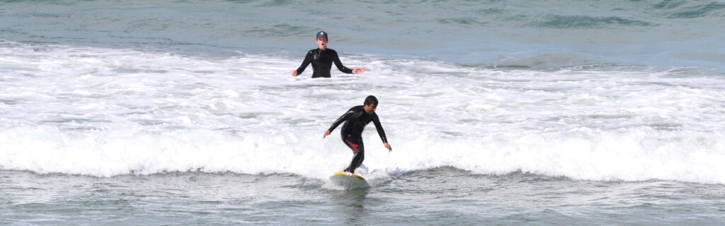Erdem standing in a surf board with trainer behind him with surprised face.