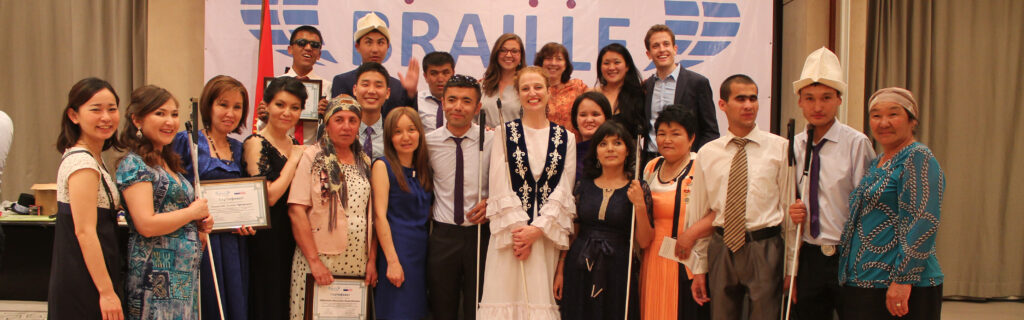 Serena Olsen standing with her Empower Blind People Kyrgyz blind students wearing a traditional Kyrgyz dress holding her white cane.