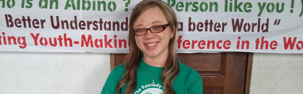 Patricia sits in front of a banner describing the goals of her alumni project.