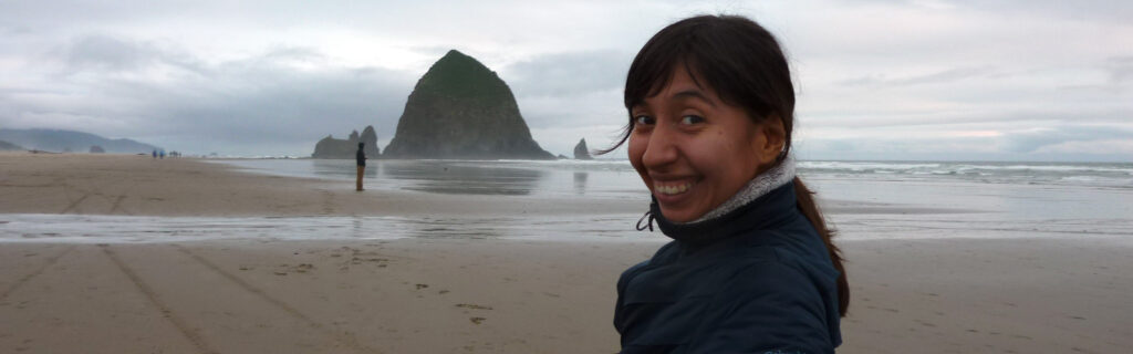 A young woman (Reveca) smiles over her shoulder with coastline in the background