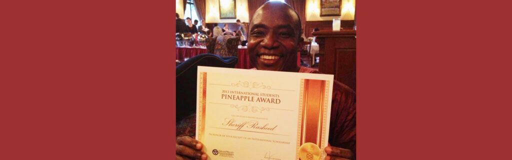 Sheriff, with a big smile, holding an award that says "2013 International Stduents Pineapple Express Award - Sheriff Rasheed"