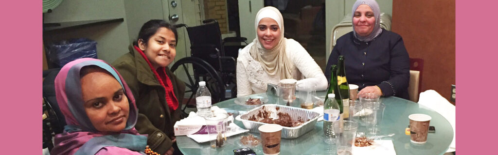 Four women sit around a table with leftover plates and cups; Three of the women wear traditional garments from their home countries