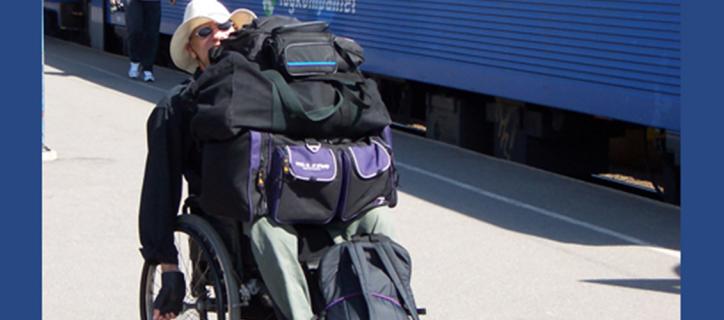 A man pushes himself in his manual wheelchair with luggage on top his lap at a Swedish train station