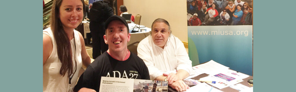 A young man wearing an ADA t-shirt displays a magazine that features him. A man and woman sit on either side. dev.miusa.org banner appears.