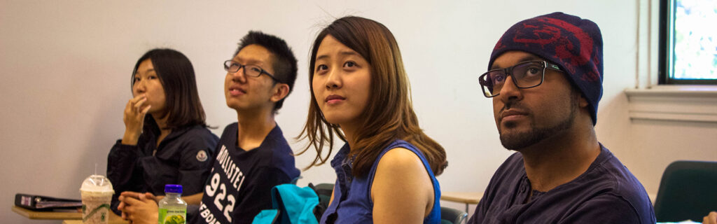 4 international students sitting in desks next to each other looking up to the front of the classroom.
