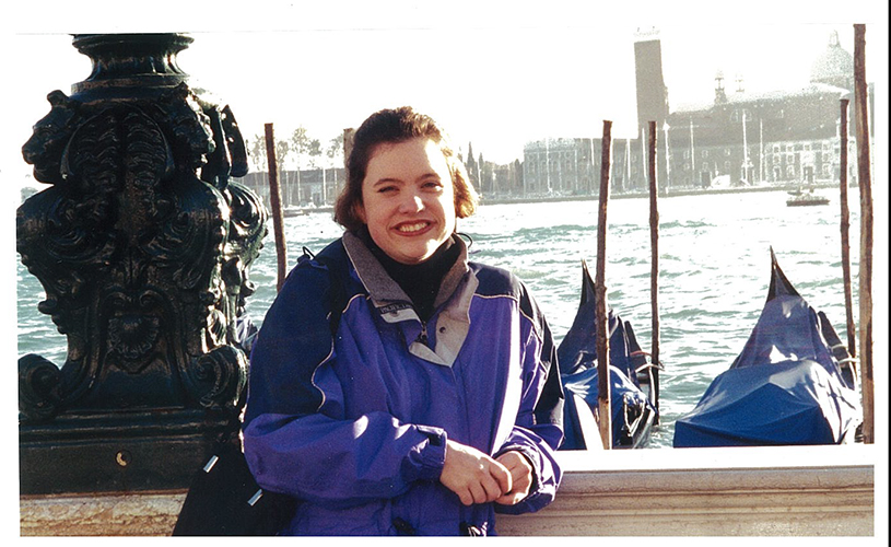 Jessica smiling leaning on bridge overlooking river and gondolas.