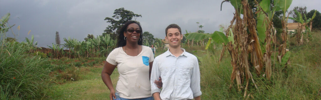 A blind woman of color holds the arm of a young man as they walk through a lush green field