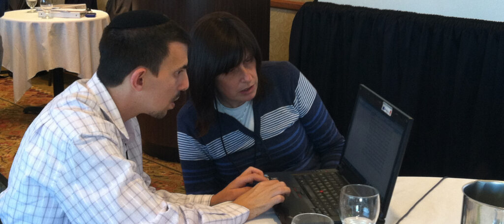 Student and teacher look at laptop screen together at table.