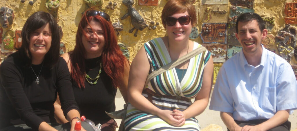 Young man sits outside with professional exchange staff in front of wall art.