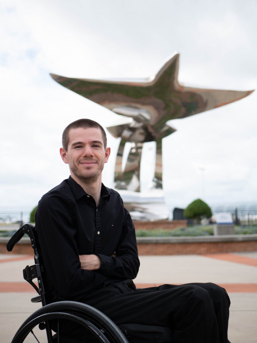 Sergio Taleisnik, who is a wheelchair user, poses outside in front of a large, metal structure.