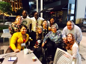 Group photo of a dozen people - including women and men, people with physical disabilities, non-disabled people, and people of color. Two women in the center are identifiable as Susan Sygall and Judy Heumann.