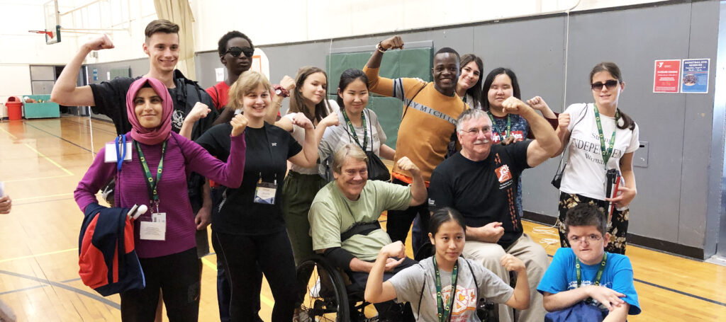 Group of high school students with disabilities representing different races, countries, cultures, smiling on basketball court as a group next to older man in wheelchair