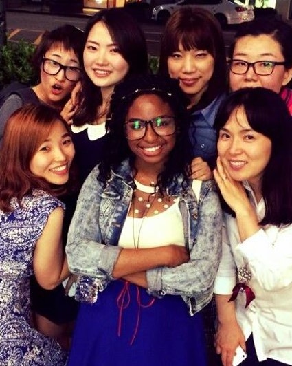 Michelle is a young black woman smiling at camera surrounded by a group of Korean friends