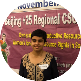 A woman from India who is blind smiles standing in front of a banner for the Beijing +25 Regional CSO forum.
