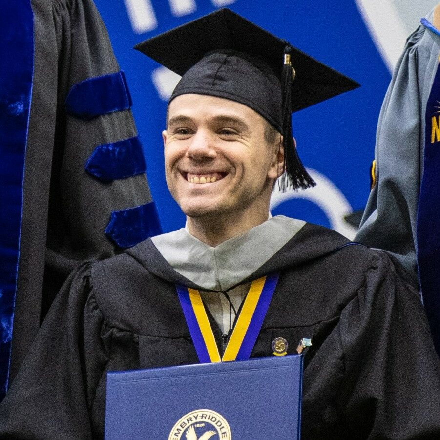 Sergio, dressed in cap and gown, smiles while receiving his Master's Diploma during his commencement ceremony.