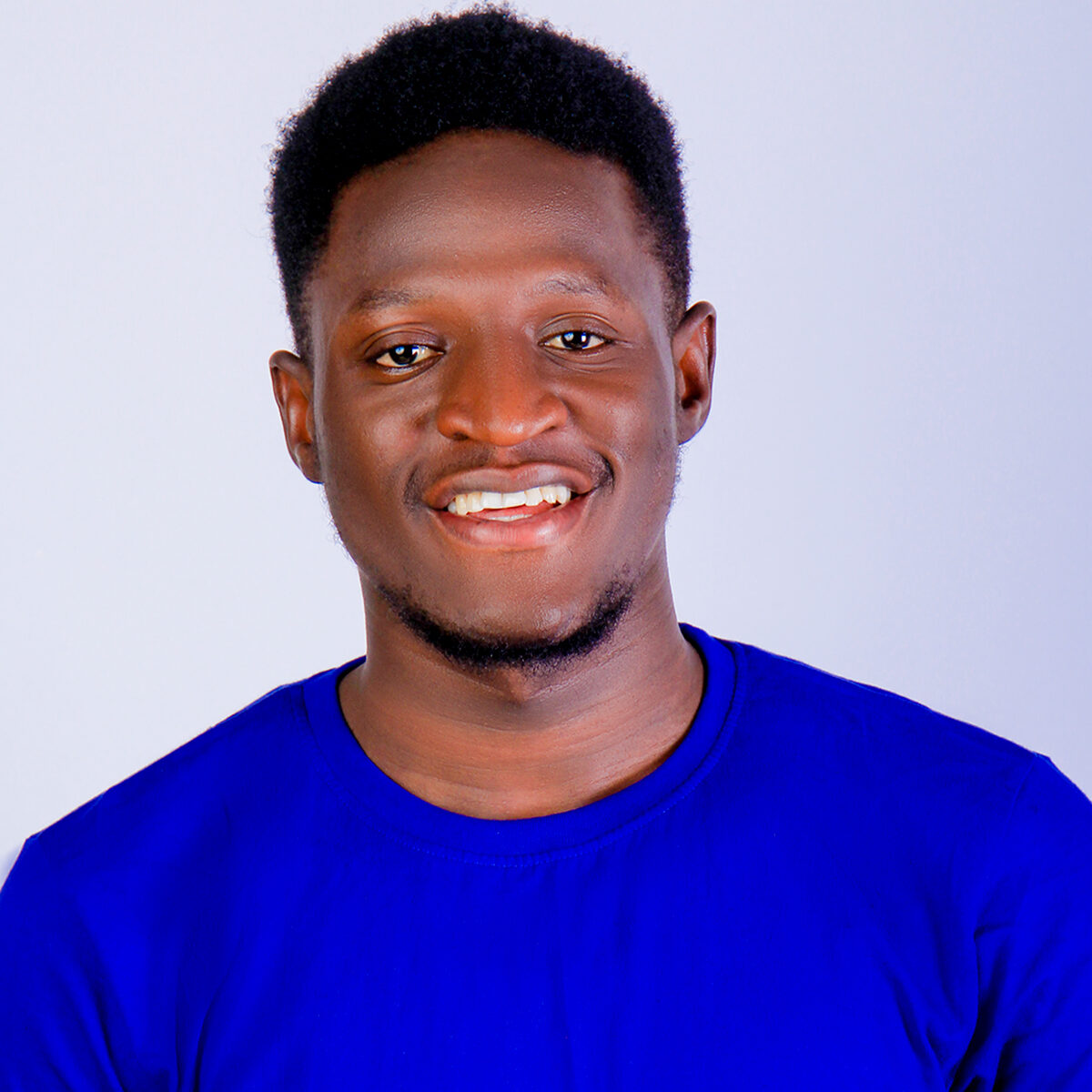 Portrait of Nehemiah a young black man wearing a blue t-shirt in a plain background and smiling at the camera.