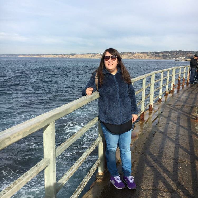 Zynep stands at a coast blue waters behind.