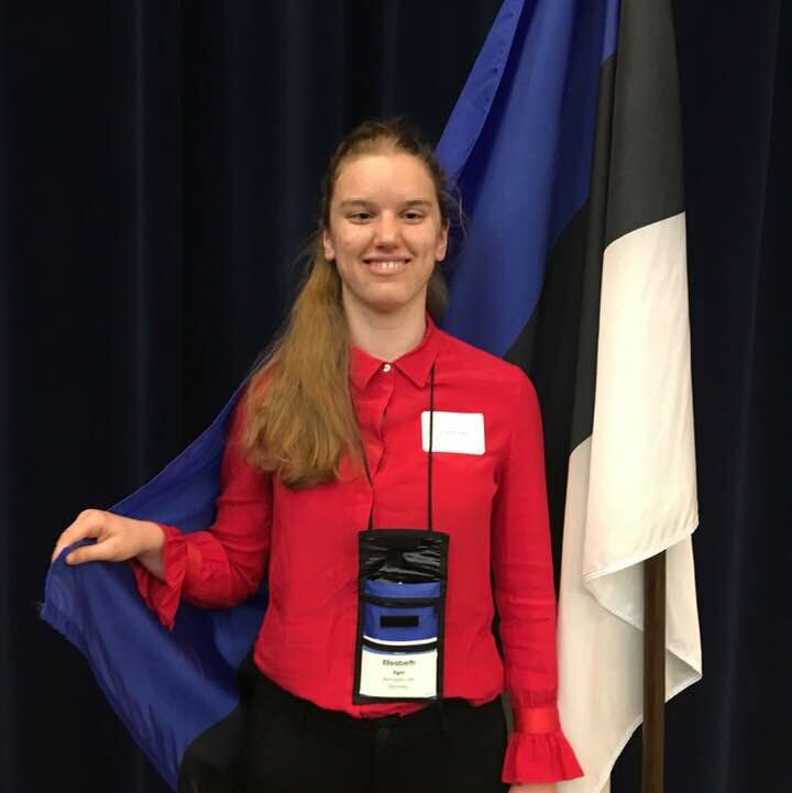 Elizabeth Stands in a in front of a flag.