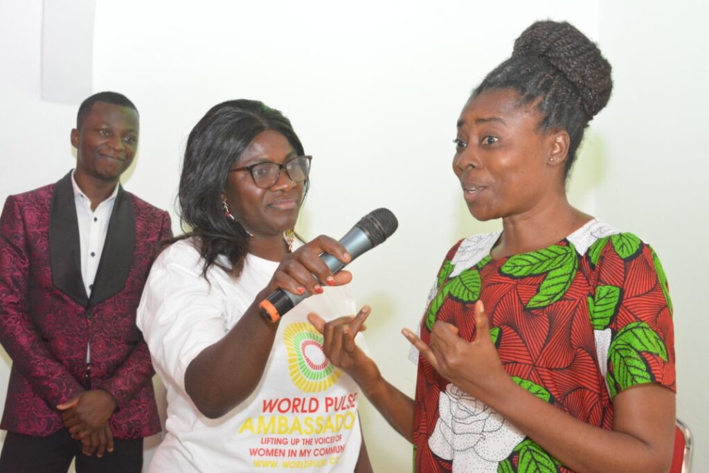 An African woman (Arrey Echi) speaks into a microphone being held by another person. She is using her hands to communicate with sign language.