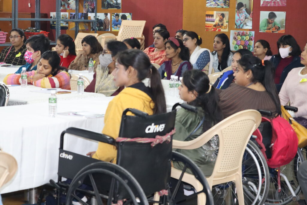 Women with various disabilities, including several women using wheelchairs, sit around a large table during a WILD-India presentation.