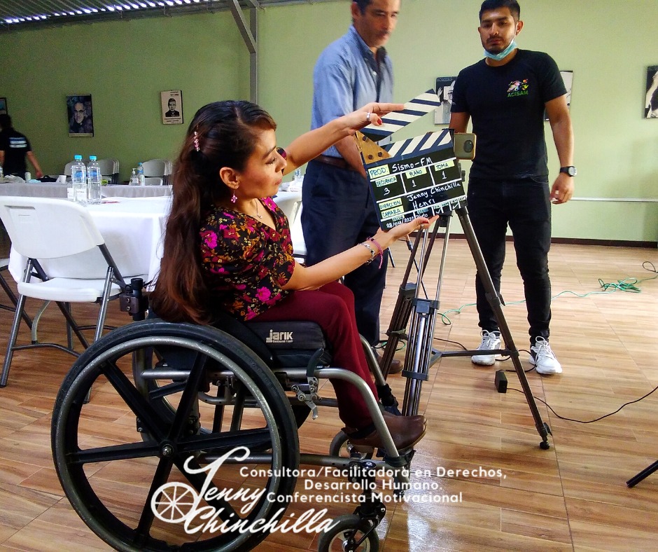 Jenny Chinchilla holds a clapperboard during filming of the documentary. Two men are standing in front of her setting up a tri-pod.