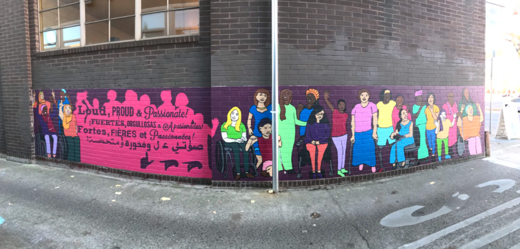 The mural covers a 30 feet wide by 5 feet high portion of a brick wall in the alleyway adjacent to Full City coffee, on Full City’s Pearl street side. Approximately half (the left half) of the mural shows a crowd of people in hot pink silhouette filled with a dark purple text that matches the dark purple background.