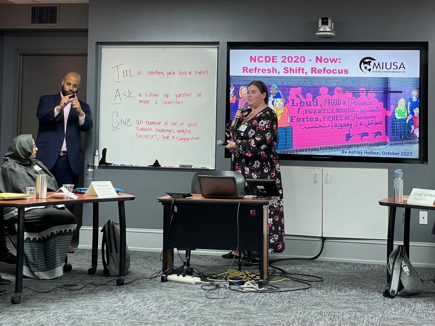 Lindsey presents speaking into a microphone to unseen audience. A sign language interpreter interprets for her.