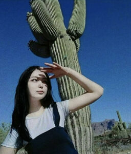 Azzaya, an alumna from Mongolia, stands in front of a cactus with her hand blocking the sun.
