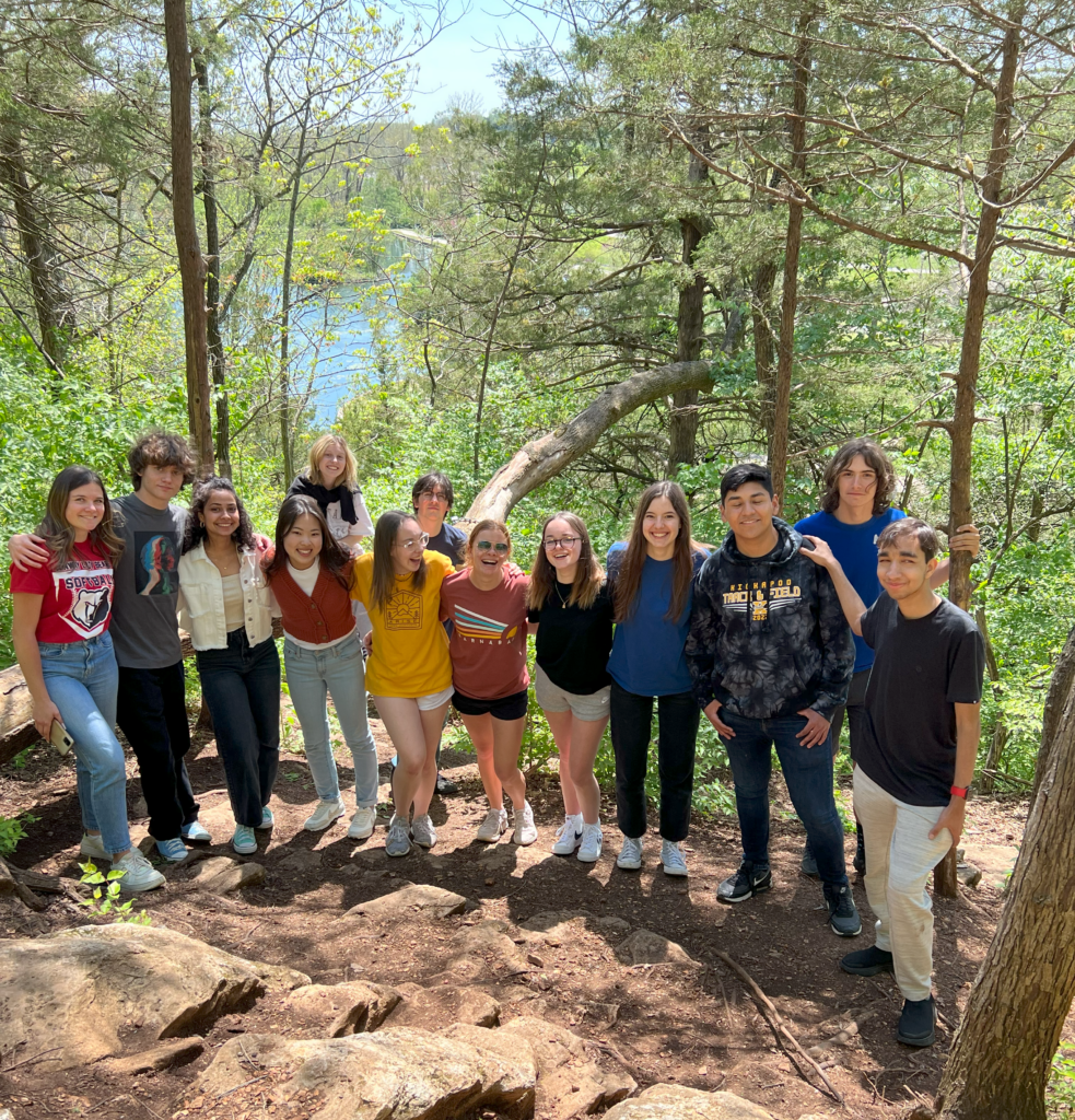 Group of high school exchange students standing on rocky surface in a park with trees behind them.
