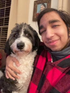 Close up of Sayed, a young Bahraini man, with his arm around a grey and white dog.