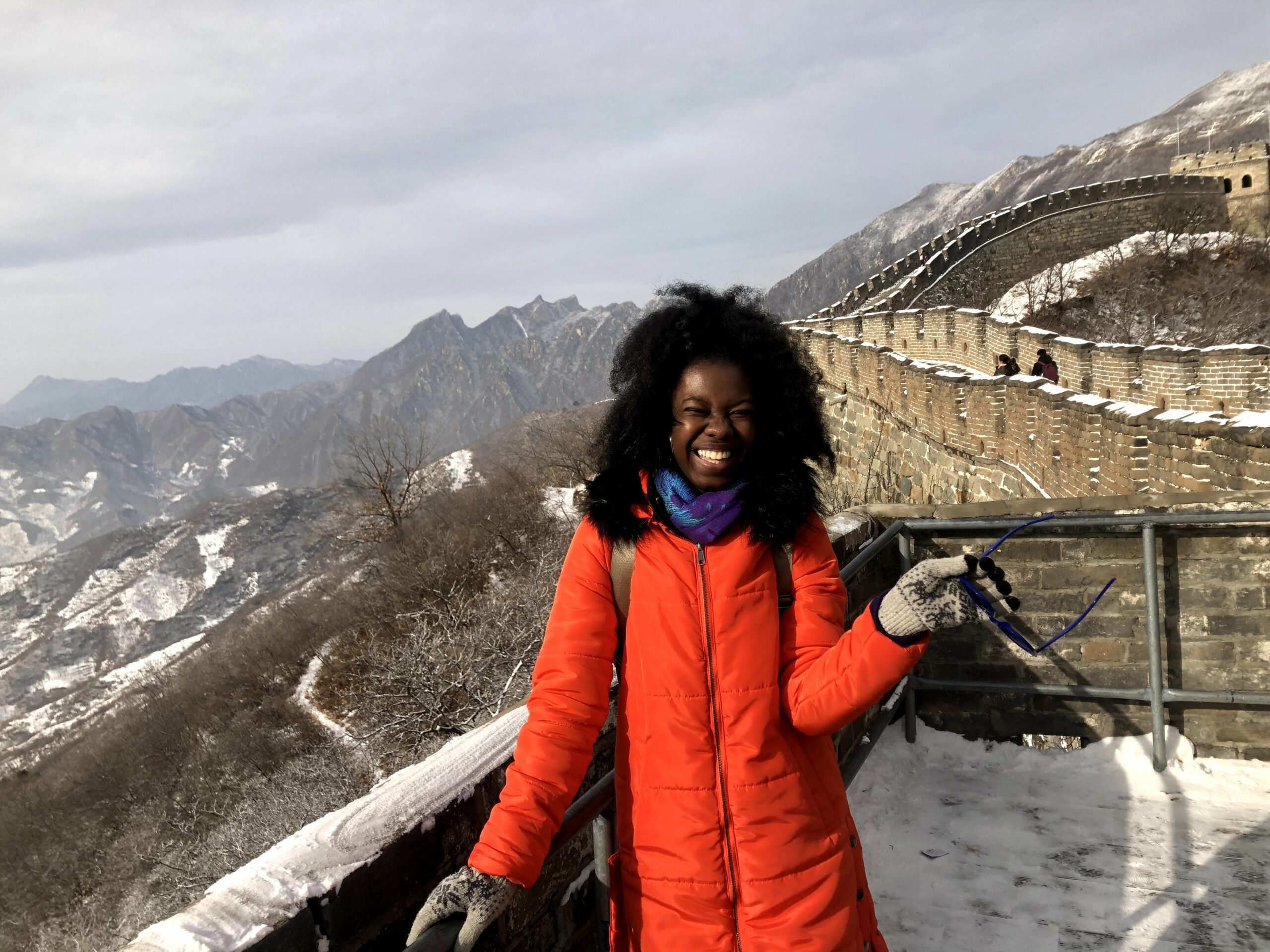 Jaelyn is a young black woman dressed in warm red coat smiling at camera while standing on the Great Wall of China covered in snow