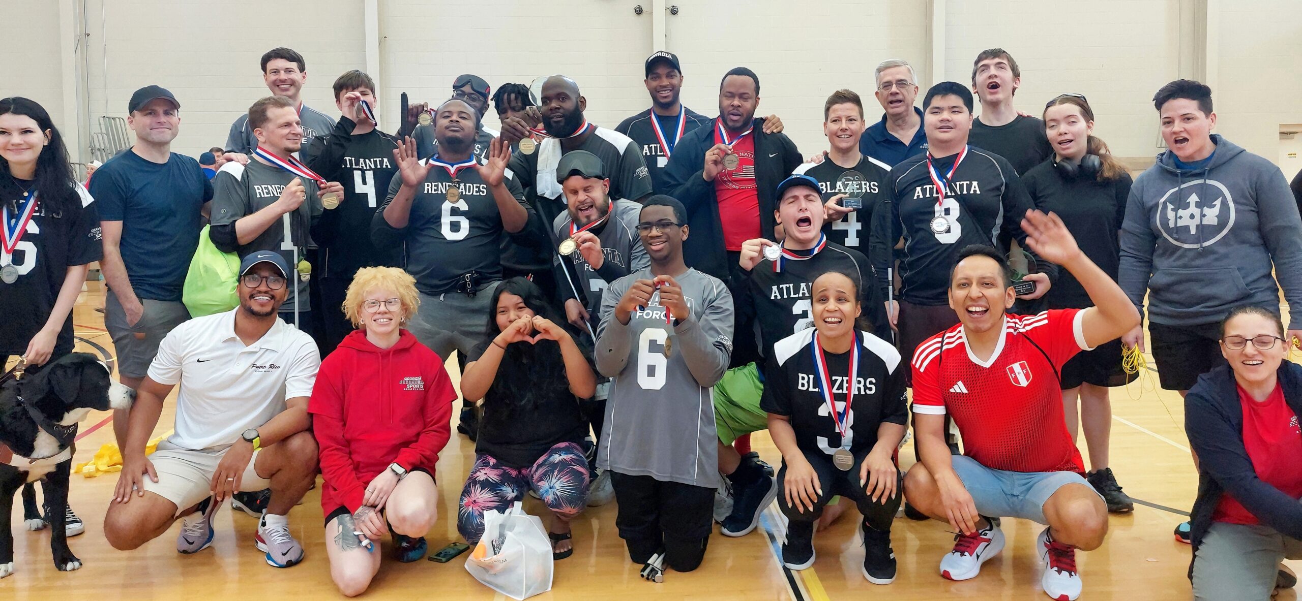 Michael Saravia crouches in the front row of a group of about 50 people posing for a group photo, mostly people who are blind or visually impaired, who are wearing athletic clothes and smiling