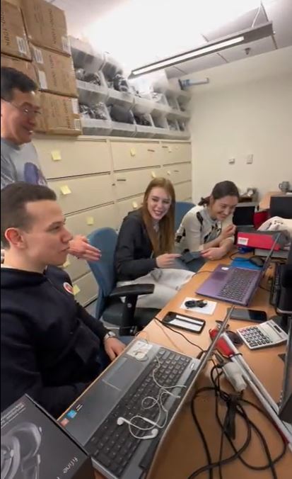 A behind the scenes photo of FLEX and YES alumni seated in front of computers and working on their podcasts as a workshop staff member stands behind them.