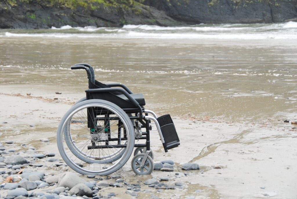 A manual wheelchair in the sand with ocean waves in the background.