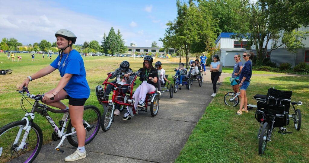 Students riding adaptive cycles single file on a bike path.