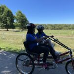 FLEXYES 2022 two people using a tandem bike together outside Two young black people smiling while riding a two-person bike outside.