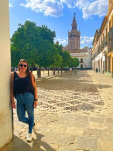Bethany stands in front of a courtyard with a bell tower in background